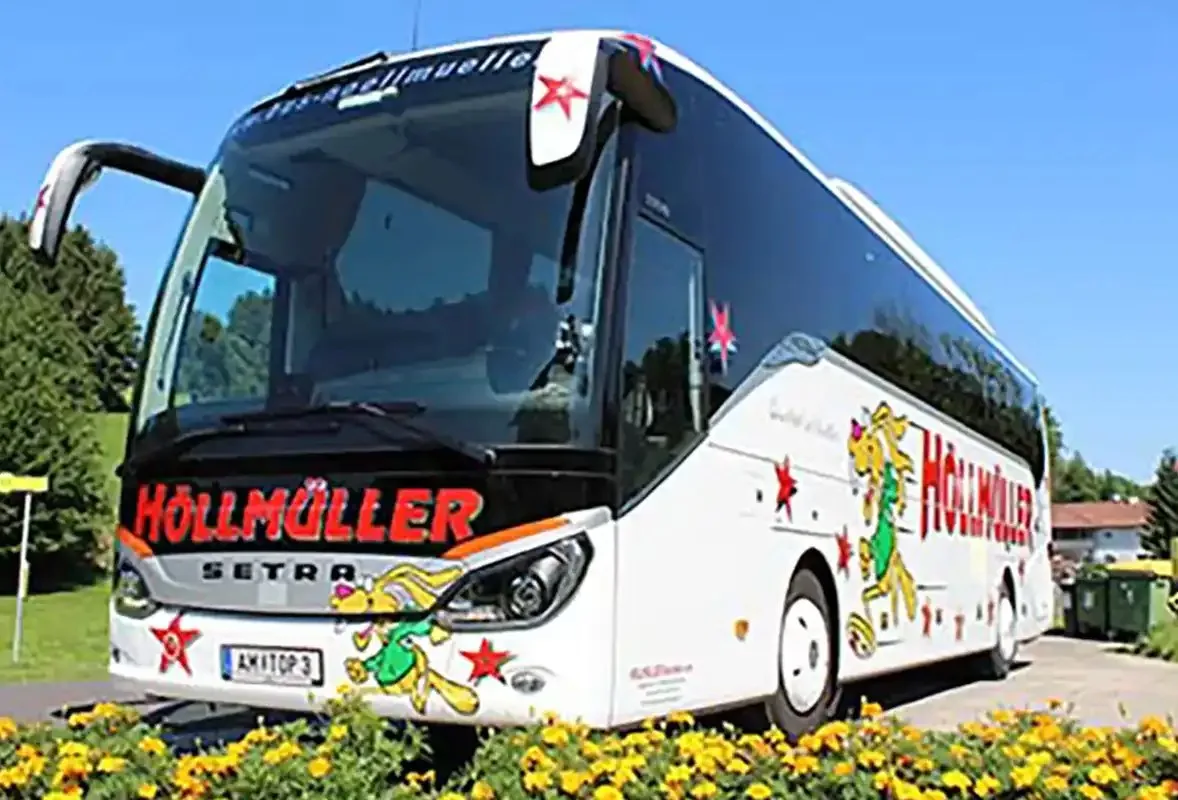 Höllmüller-Reisebus von Setra von vorne, davor ein gelb blühendes Blumenbeet