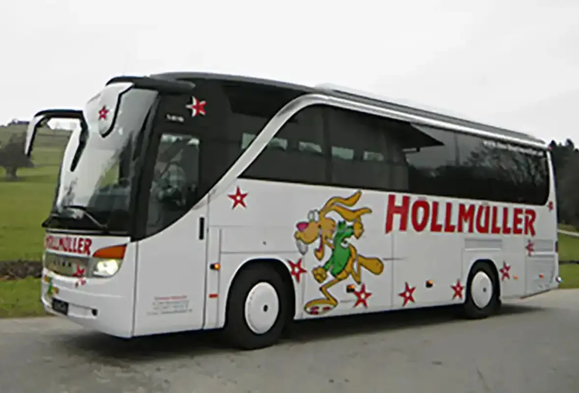 Weißer Höllmüller-Reisebus mit roten Sternen und Hase seitlich vor grauem Himmel