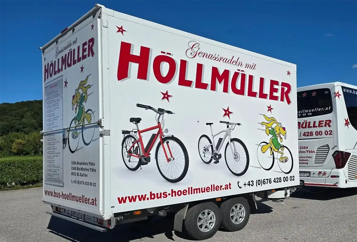 Bikeliner-Radanhänger mit der Aufschrift „Genussradeln mit Höllmüller“ und gezeichneten Fahrrädern